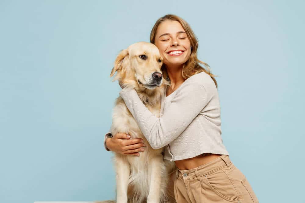 Eine Frau umarmt einen großen Hund vor einem blauen Hintergrund.